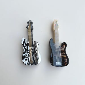 Peut inclure: Deux objets décoratifs en forme de guitare. L'un présente un motif zébré noir et blanc, l'autre est noir avec un motif tacheté. Les deux ont un manche et une tête clairs avec des cordes et des chevilles.