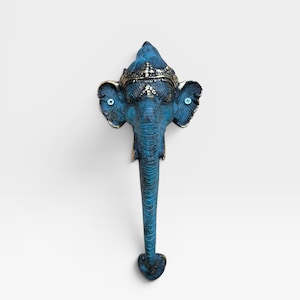 May include: A blue and bronze-toned metal door handle shaped like an elephant head. The elephant features a detailed crown, large ears with visible screw heads, and a long, downward-curving trunk that forms the main grip of the handle.