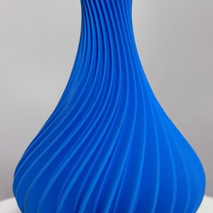 Könnte beinhalten: Eine leuchtend blaue Vase mit einem einzigartigen, spiralförmigen Design. Die Vase hat einen breiten Boden, der sich zu einem schmalen Hals verjüngt, mit vertikalen Rippen, die ein strukturiertes, auffälliges Muster bilden. Geeignet für die Inneneinrichtung.