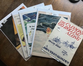May include: A collection of vintage paper ephemera, including advertisements and sheet music. The sheet music cover reads "The Caissons Go Rolling Along" with a blue illustration. Other items feature aviation and wartime themes.