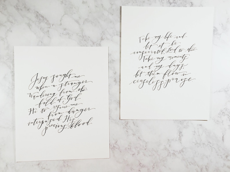May include: Two black and white calligraphy prints with inspirational quotes. The first print reads "Jesus sought me when a stranger wandering from the fold of God He to rescue me to from danger interposing His precious blood." The second print reads "Take my life and let it be consecrated, Lord, to thee. Take my moments and my days, let them flow in ceaseless praise."