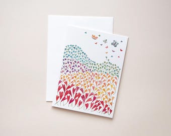 May include: A greeting card with a watercolor design of colorful hearts and butterflies. The hearts transition from red to yellow to blue. A white envelope is behind the card.