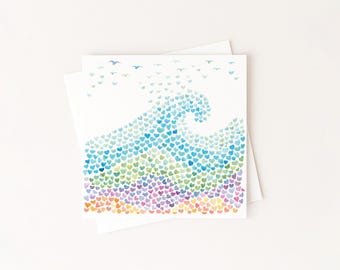 May include: A square greeting card featuring a watercolor illustration of an ocean wave composed of numerous small, multicolored hearts in shades of blue, green, purple, orange, and yellow, with small bird silhouettes flying above the wave.
