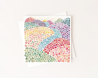 May include: A square greeting card featuring a watercolor illustration of a landscape composed entirely of small, multicolored hearts. The scene depicts rolling hills, a winding path, and a rising sun, rendered in shades of green, blue, pink, and yellow.