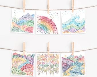 May include: Six square art prints hanging on a twine string with wooden clips. Each print features a landscape or scene composed of tiny, multicolored watercolor hearts, including mountains, a rainbow, ocean waves, rolling hills, and a forest.