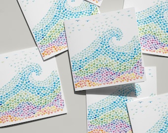 May include: A collection of square greeting cards featuring a watercolor illustration of a wave composed of tiny multicolored hearts. The design transitions from warm orange and pink at the base to cool blue and green at the crest, with small birds.