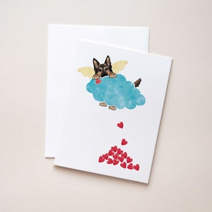 May include: A greeting card featuring a cartoon German Shepherd dog with angel wings holding a red heart while flying in a blue cloud. Red hearts are falling from the cloud.