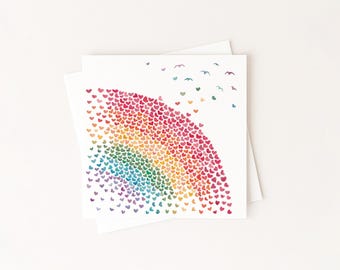 May include: Two white greeting cards with a watercolor design. The design features a rainbow arc made of small hearts in various colors, with small birds flying above. The cards are on a white background.