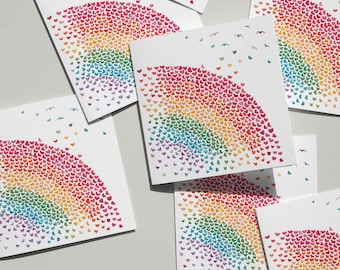 May include: A collection of square white greeting cards featuring a rainbow arc composed of small, multicolored heart-shaped illustrations. Each card displays a gradient of red, orange, yellow, green, blue, and purple hearts with small birds.