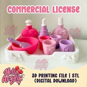 Puede incluir: Una bandeja rectangular blanca que contiene una colección de objetos cosméticos impresos en 3D en rosa y morado, incluyendo una botella en forma de corazón, un labial, una botella con lazo, un cuenco con brocha y vasos pequeños. Texto COMMERCIAL LICENSE.