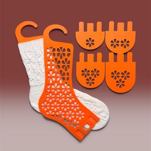 May include: An orange plastic sock blocker with a floral cutout pattern, holding a white knit sock. Four additional orange plastic heel and toe inserts are included, labelled with size ranges 37-38, 39-40, 41-42, and 43-44, each featuring floral cutouts.