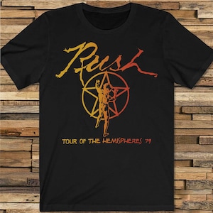 May include: Black t-shirt featuring the band name "Rush" in yellow and orange script. Below the name is a graphic of a figure inside a star, with the text "TOUR OF THE HEMISPHERES 79".