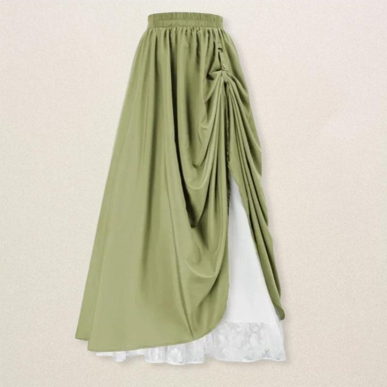 May include: A flowing, olive green skirt with a draped design. The skirt features a high waist and a side slit, revealing a white underskirt with a lace hem. The fabric has a soft, elegant drape, suitable for formal or special occasions.