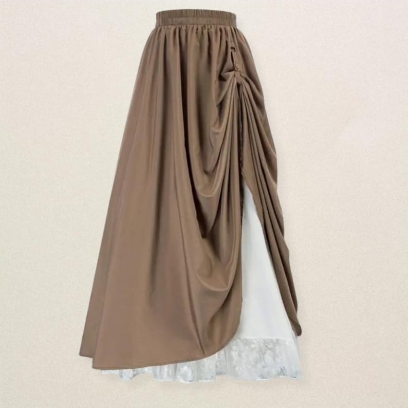 May include: A long, brown skirt with a draped design and a high waist. The skirt features a side slit revealing a white underlayer with a lace trim. The fabric has a flowing, elegant appearance.