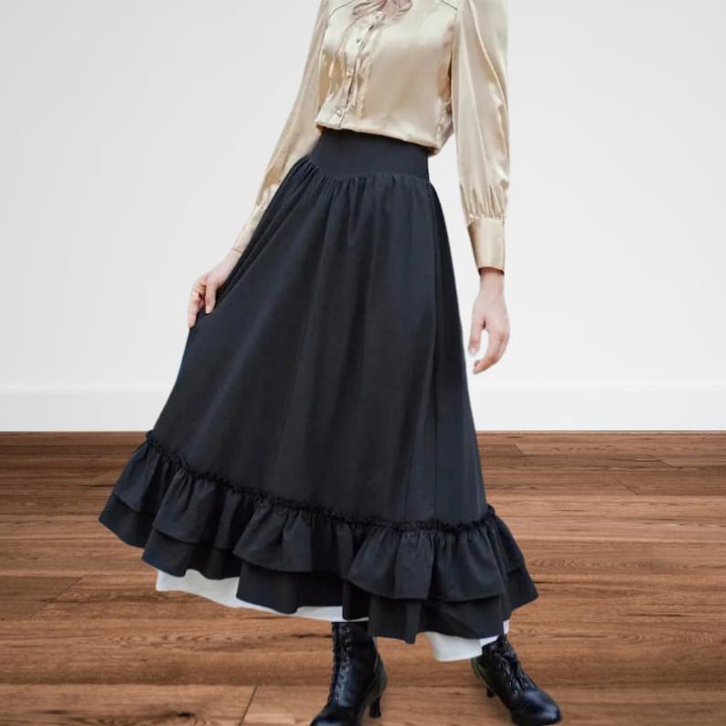 May include: A long black skirt with a high waist and ruffled hem. The skirt is paired with a gold-colored blouse with long sleeves. Black ankle boots complete the outfit. The skirt appears to be made of a flowing fabric.