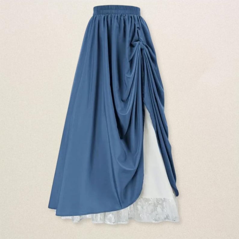 May include: A flowing, dusty blue skirt with a draped design. The skirt features a high waist and a split that reveals a white underskirt with a lace hem. The fabric has a soft, elegant drape.