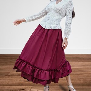 May include: A two-piece outfit featuring a white lace top with long sleeves and a V-neck, paired with a long, flowing burgundy skirt. The skirt has a ruffled hemline. The outfit is suitable for a formal event or a vintage-inspired look.