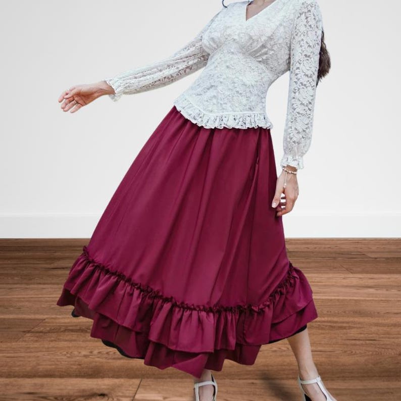 May include: A two-piece outfit featuring a white lace top with long sleeves and a V-neck, paired with a long, flowing burgundy skirt. The skirt has a ruffled hemline. The outfit is suitable for a formal event or a vintage-inspired look.