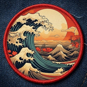 May include: Round embroidered patch featuring a Japanese wave design with a red border. The artwork depicts a large wave, a setting sun, and mountains in shades of blue, orange, and brown. The patch is sewn onto a blue denim fabric.