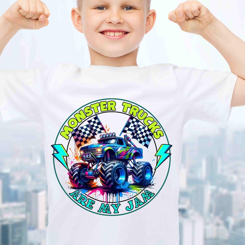 Puede incluir: Camiseta blanca con un gr&aacute;fico colorido de un monster truck, banderas a cuadros y el texto "MONSTER TRUCKS ARE MY JAM" en un dise&ntilde;o circular. El monster truck es azul, con neum&aacute;ticos grandes y un vibrante efecto de salpicaduras de pintura.