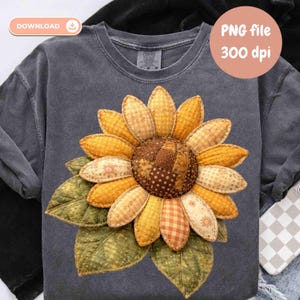 Pode incluir: Uma camisa cinza de manga comprida com um grande design de girassol aplicado. O girassol tem pétalas amarelas e laranja com um centro de patchwork. As folhas verdes estão na base da flor. O texto "PNG file 300 dpi" está em um círculo.