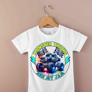 Puede incluir: Camiseta blanca con un dise&ntilde;o de cami&oacute;n monstruo colorido. El gr&aacute;fico incluye el texto "MONSTER TRUCKS ARE MY JAM" en un dise&ntilde;o circular con banderas a cuadros y rayos. El cami&oacute;n es azul, morado y verde.