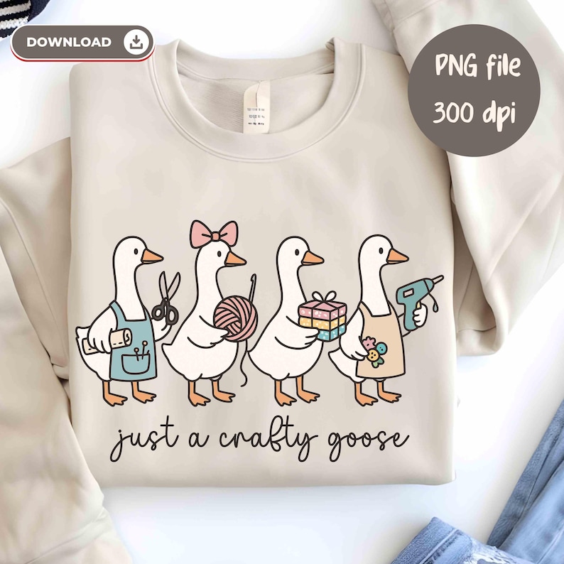 May include: Beige sweatshirt featuring a whimsical illustration of four geese, each holding craft supplies like scissors, yarn, and a glue gun. The text "just a crafty goose" is written below the geese. The image also includes the text "PNG file 300 dpi".