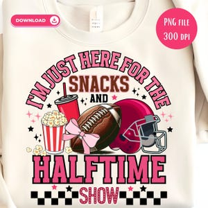 May include: Cream-colored sweatshirt with a graphic design featuring a football, helmet, popcorn, and a drink. The text reads "I'm just here for the snacks and halftime show" in pink and black.