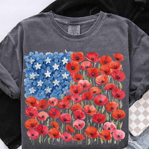 May include: Dark grey sweatshirt with a floral American flag design. The flag features blue flowers and white stars in the upper left, with red poppies filling the rest of the flag.