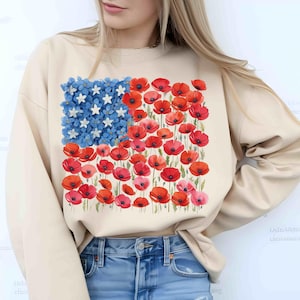 May include: Beige sweatshirt with a floral American flag design. The flag features blue flowers and white stars in the upper left, and red poppies for the stripes. A patriotic floral themed garment.