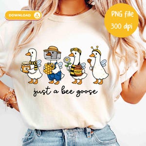 May include: Cream-colored t-shirt featuring a whimsical illustration of four geese dressed as bees and beekeepers. Each goose holds honey-related items. The text "just a bee goose" is printed below the geese. A yellow circle indicates a PNG file.