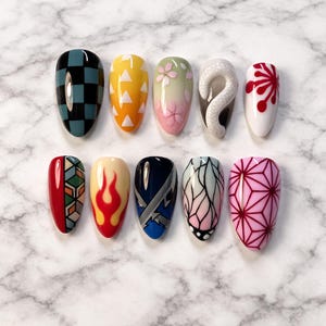 May include: A set of ten artificial nails with various designs. The designs include a black and teal checkerboard, yellow triangles, pink cherry blossoms, a white snake, red floral patterns, geometric shapes, flames, blue and silver accents, butterfly wings, and pink geometric patterns.