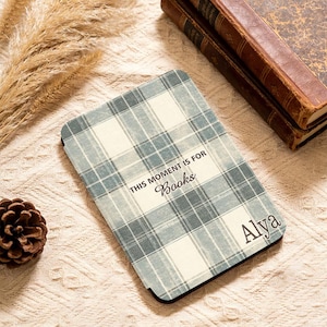 Könnte beinhalten: Ein rechteckiger Buchumschlag mit blauem und weißem Karomuster. Der Text "THIS MOMENT IS FOR Books" ist auf dem Umschlag aufgedruckt, zusammen mit dem Namen "Alya". Der Umschlag liegt neben zwei alten Büchern.