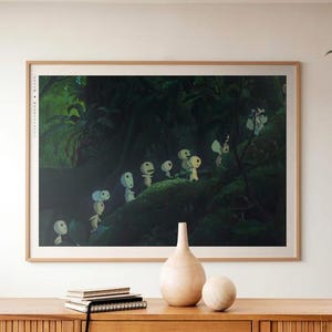 May include: A framed print depicting a forest scene with small, white, humanoid figures. The artwork is set against a dark green background, with a light brown wooden frame. The print is displayed on a wooden cabinet with decorative items.