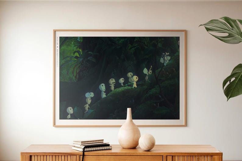 May include: A framed print depicting a forest scene with small, white, humanoid figures. The artwork is set against a dark green background, with a light brown wooden frame. The print is displayed on a wooden cabinet with decorative items.
