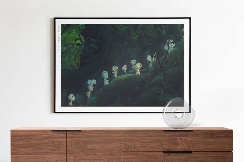 May include: A framed art print depicting a forest scene with several small, white, humanoid figures with large heads. The artwork is set against a dark green background. The print is displayed above a wooden cabinet, adding a touch of nature.