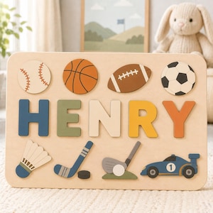 May include: A rectangular wooden name puzzle featuring the name HENRY in large, colorful block letters. The board includes cutouts for a baseball, basketball, football, soccer ball, badminton shuttlecock, hockey stick, golf club, and race car.