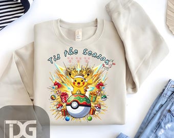 May include: Beige sweatshirt featuring a Pikachu character wearing a Santa hat, standing on a Poké Ball ornament. The design includes the text "Tis the Season" and festive elements like presents and Poké Balls. A cozy, long-sleeved top.