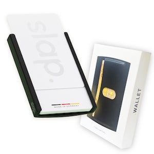 Può includere: Un portafoglio nero con interno dorato e una scatola bianca con la scritta "WALLET" stampata sul lato. Il portafoglio è esposto accanto a un porta carte bianco con la scritta "slap." stampata sopra, e le parole "MADE IN GERMANY" sono stampate in basso.