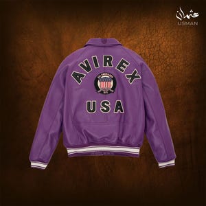 May include: A purple leather jacket with the word "AVIREX" arched across the back, above a circular patch with the American flag and the text "ALL AMERICANS 1975". The word "USA" is below the patch. The jacket has white and black striped cuffs.