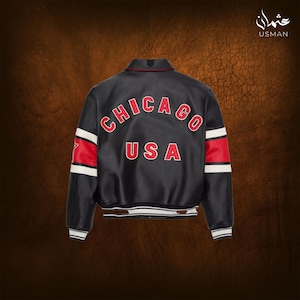 Puede incluir: Chaqueta de cuero negra con letras rojas "CHICAGO USA". La chaqueta tiene rayas rojas y blancas en las mangas y un dobladillo a rayas blanco y negro. El cuello es rojo. La chaqueta es de estilo bomber.