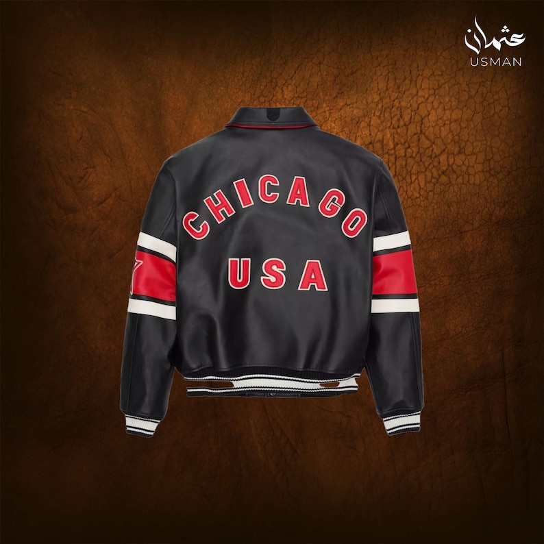 Puede incluir: Chaqueta de cuero negra con letras rojas "CHICAGO USA". La chaqueta tiene rayas rojas y blancas en las mangas y un dobladillo a rayas blanco y negro. El cuello es rojo. La chaqueta es de estilo bomber.