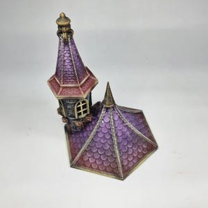 以下が含まれることがあります： 紫と赤のミニチュア装飾城塔。尖った屋根と小さな窓があります。塔は詳細なデザインと金色の飾りを持っています。屋根は鱗模様でテクスチャ加工されています。