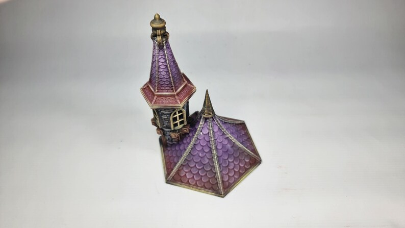 以下が含まれることがあります： 紫と赤のミニチュア装飾城塔。尖った屋根と小さな窓があります。塔は詳細なデザインと金色の飾りを持っています。屋根は鱗模様でテクスチャ加工されています。