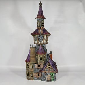 以下が含まれることがあります： 高い塔と複数のレベルを備えた、詳細なミニチュア城。 城は紫色の屋根、石壁、小さな窓が特徴です。 全体的なデザインは気まぐれで装飾的で、展示に適しています。