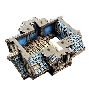 Puede incluir: Maqueta de edificio en miniatura y desgastada, con un suelo de madera detallado y paredes interiores azules. El tejado est&aacute; cubierto de tejas grises, y el exterior presenta texturas de madera y piedra envejecidas. Se ven ventanas.