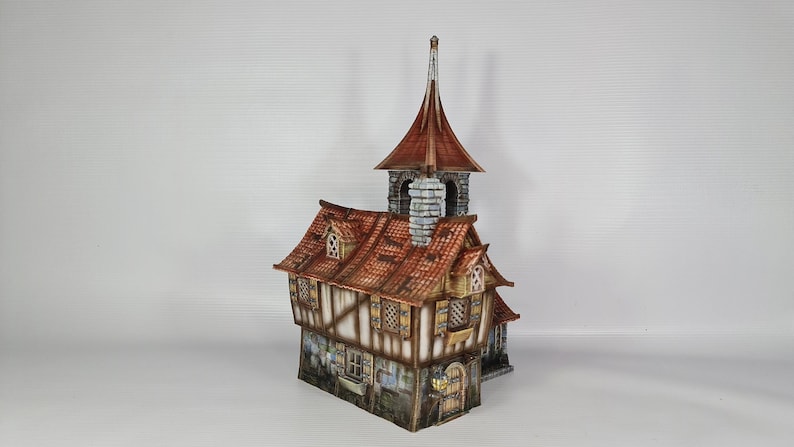 May include: A detailed miniature model of a medieval-style building. The structure features a red-tiled roof, a tall steeple, and multiple windows with shutters. The building is painted in shades of brown, beige, and grey, creating a realistic appearance.