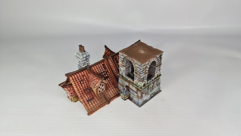 May include: A detailed miniature building model featuring a red-tiled roof, a stone tower, and a chimney. The roof includes a dormer window. The tower has arched openings and a flat roof. The model is painted with realistic details.