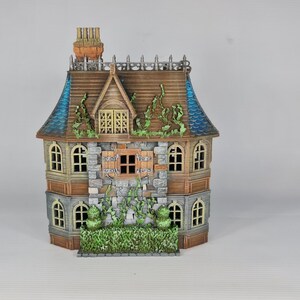 Op de afbeelding: Een gedetailleerd miniatuurhuis met een bruin dak, blauwe accenten en een stenen gevel. De ramen zijn gebogen en het huis is versierd met decoratieve wijnranken en een kleine schoorsteen. Fantasiethema.