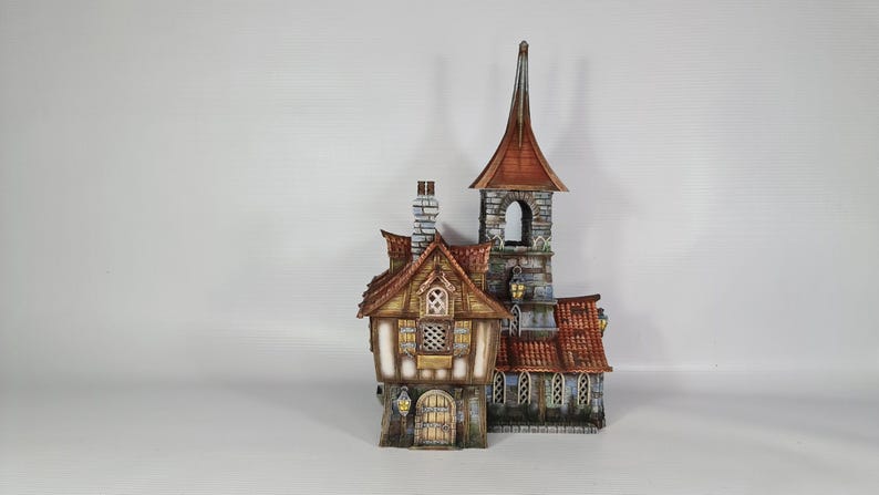 May include: A detailed miniature building with a steeple and a red-tiled roof. The structure features multiple windows, a stone facade, and a wooden door. The building has a whimsical, fairytale-like design, with a chimney and decorative lanterns.